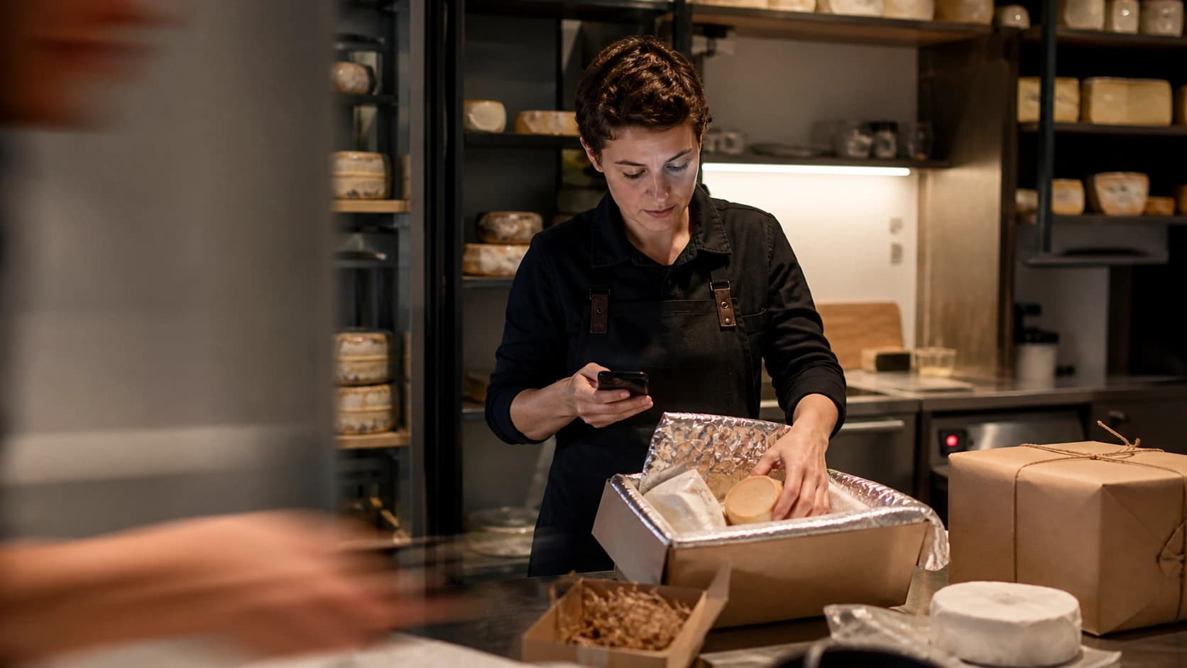 A Rosalie team member checks a phone while packing an artisan cheese order.