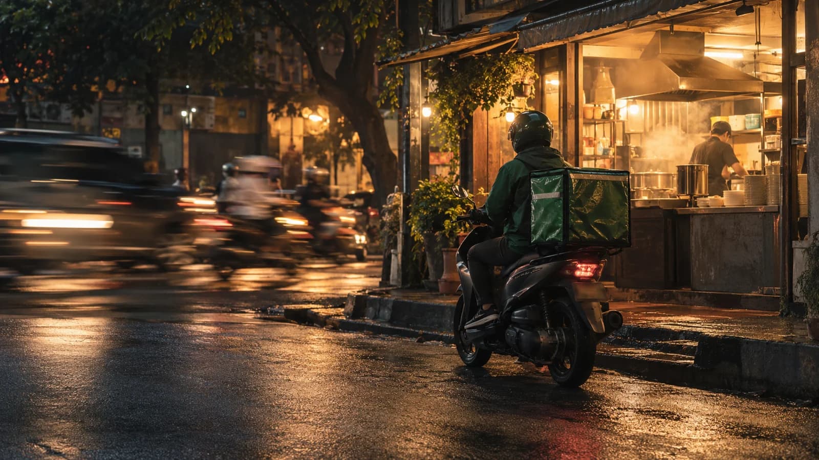 Kurir di atas motor menunggu di depan dapur hangat di Jakarta saat lalu lintas malam melintas.